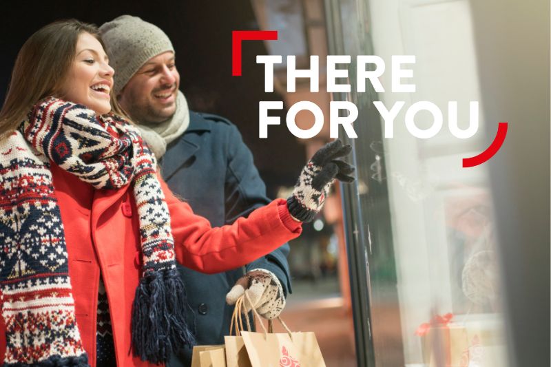 Image of man and woman, both wearing a hat, coat and scarf, looking in a shop window at Christmas Gifts